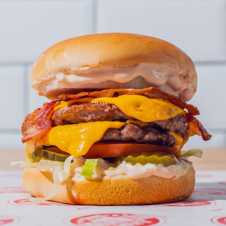 Double cheeseburger with bacon, lettuce, tomato, pickles, onions, and sauce on a toasted bun.