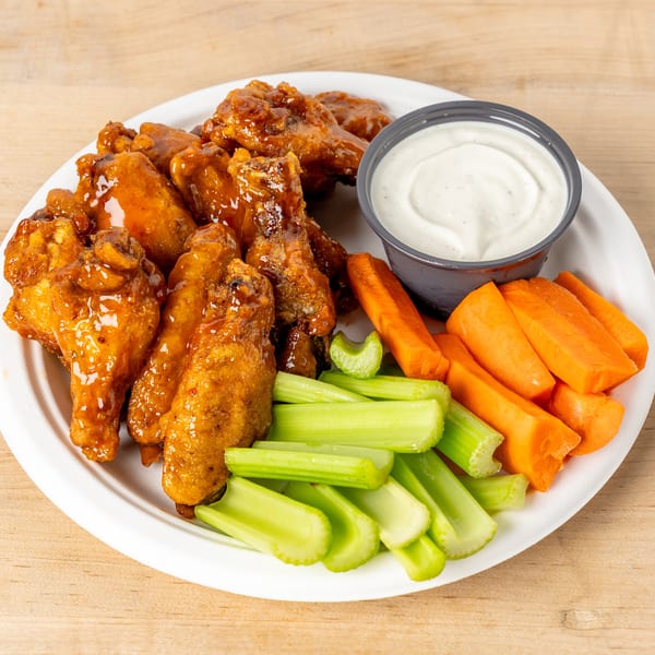 Glazed chicken wings with celery sticks, carrot sticks, and a side of ranch dressing.