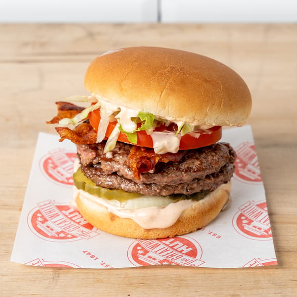 Double patty burger with bacon, lettuce, tomato, onion, pickles, and sauce on a bun.
