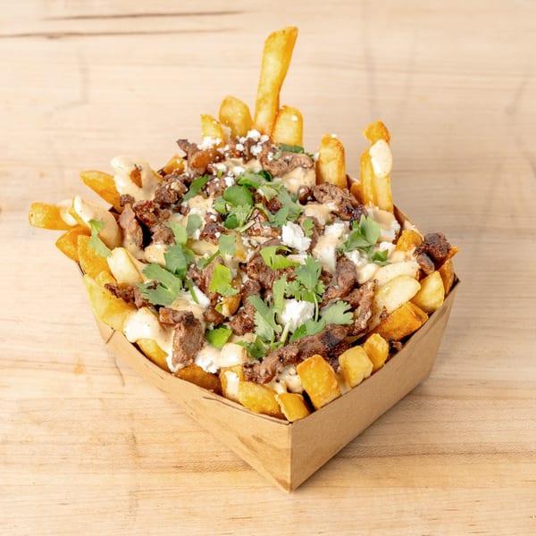 Loaded fries with steak, feta cheese, a creamy sauce, and cilantro in a cardboard tray.