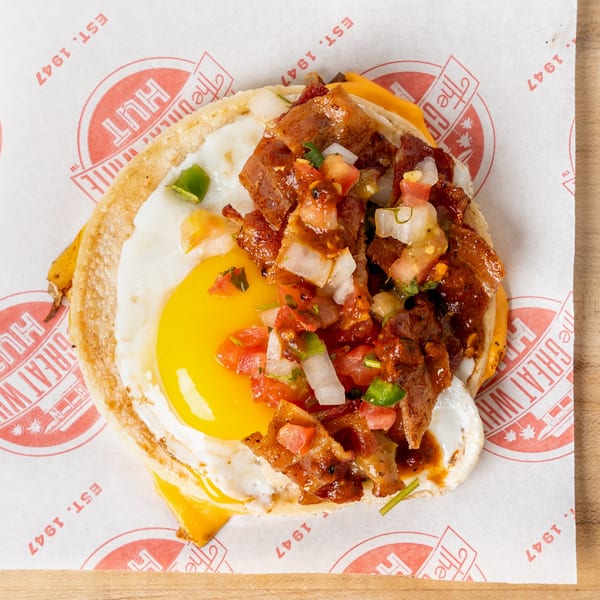 Breakfast taco with a fried egg, bacon, cheese, and pico de gallo on branded paper.