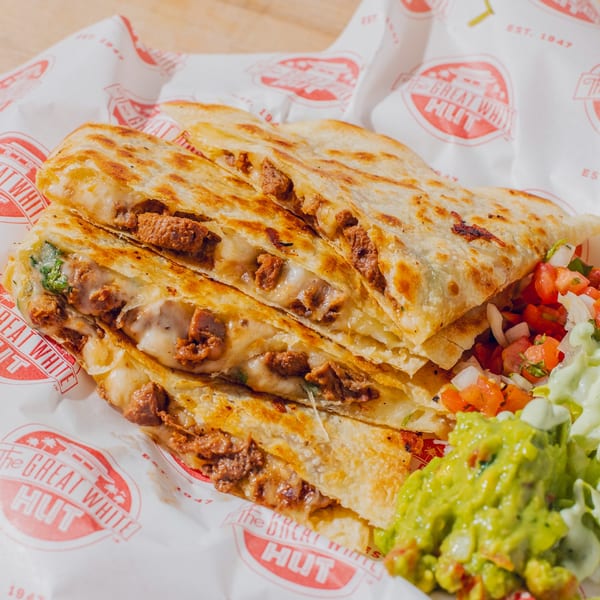 Grilled beef quesadillas with melted cheese, pico de gallo, and guacamole on branded restaurant paper.