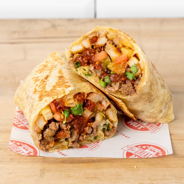 Two halves of a burrito filled with meat, potatoes, salsa, and cilantro on branded paper.