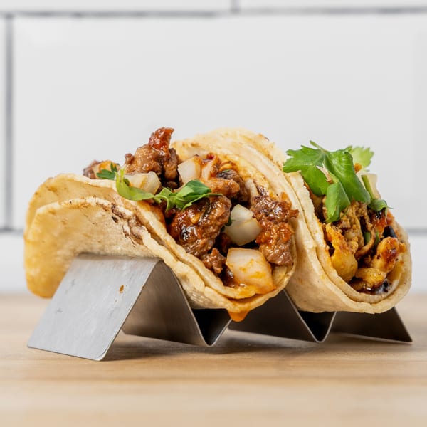 Two tacos, one with beef and onions, the other with chicken, in a metal holder.